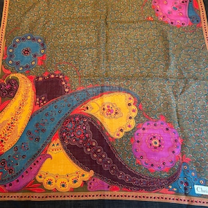 May include: A square, black silk scarf with a paisley pattern in shades of blue, yellow, pink, and red. The scarf has a brown border and a small label that reads "Chris".