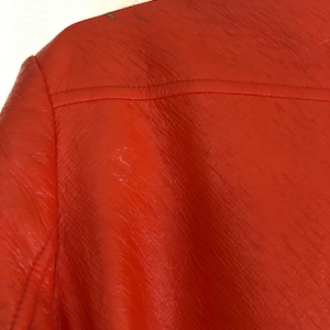 K&ouml;nnte beinhalten: Nahaufnahme einer leuchtend orangefarbenen Lederjacke. Die Jacke hat eine strukturierte Oberfl&auml;che und einen Rei&szlig;verschluss.