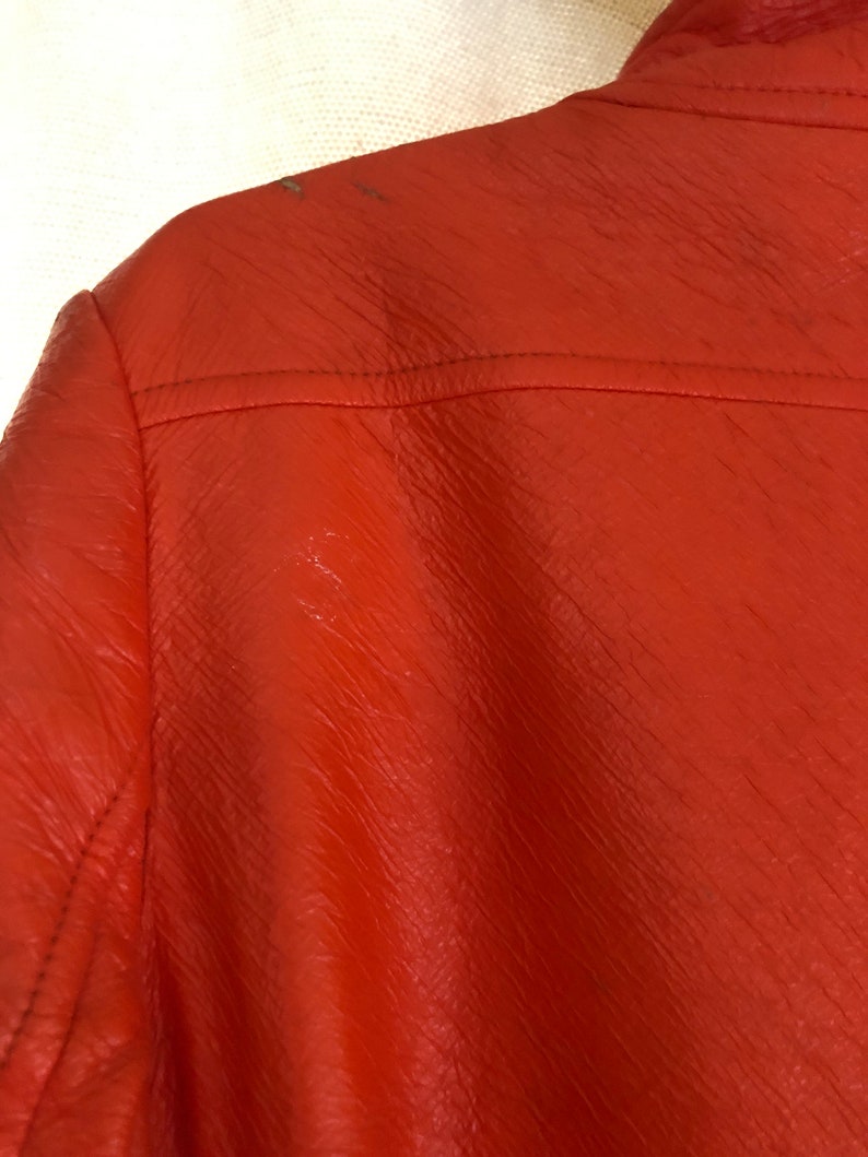 K&ouml;nnte beinhalten: Nahaufnahme einer leuchtend orangefarbenen Lederjacke. Die Jacke hat eine strukturierte Oberfl&auml;che und einen Rei&szlig;verschluss.