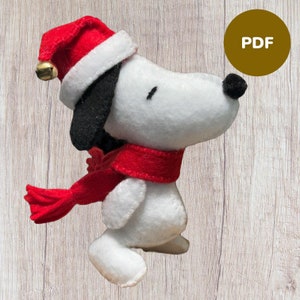 May include: A white felt plush toy of a dog wearing a red and white Santa hat and a red scarf. The toy is standing on a woodgrain background.