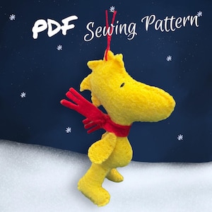 May include: A yellow felt plush toy of a dog wearing a red felt scarf. The toy is standing on a white surface with a blue background. The text "PDF Sewing Pattern" is at the top of the image.
