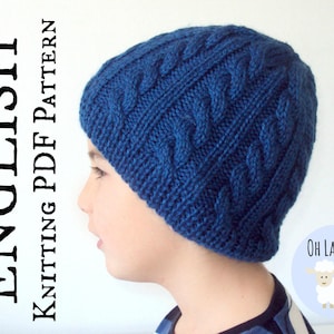 May include: A blue knitted hat with a cable knit pattern. The hat is being worn by a child. The text "Oh La Lana!" is visible in the image.