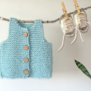 Könnte beinhalten: Eine hellblaue Strickweste mit Holzknöpfen, die an einem Ast hängt.