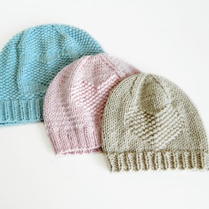 Puede incluir: Tres gorros de punto en diferentes colores: azul claro, rosa y beige. Los gorros tienen un patrón texturizado y un borde doblado.