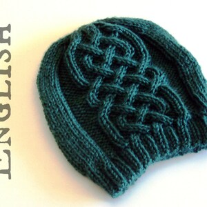 Puede incluir: Un gorro de punto verde oscuro con un patrón de trenza. El gorro tiene un ala ancha y un ajuste holgado.