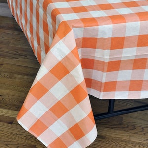 May include: Orange and white checked tablecloth. The tablecloth is made of a lightweight material and has a classic gingham pattern.