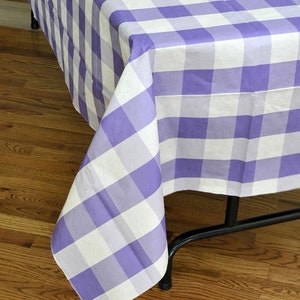 Puede incluir: Un mantel a cuadros blanco y morado con un patrón de vichy. El mantel está drapeado sobre una mesa con patas de metal negro.