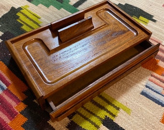 May include: A wooden valet tray with a drawer. The tray has a rectangular shape and is made of dark brown wood. The drawer is open and is also made of dark brown wood.