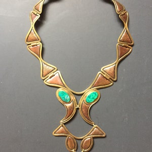 May include: A gold and copper necklace with a geometric design and green stones. The necklace is made of metal and has a unique, modern style.