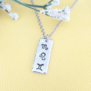 May include: Silver necklace with a rectangular tag pendant featuring the astrological symbols for Scorpio, Leo, and Gemini.