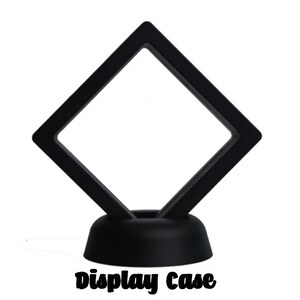 May include: Black diamond-shaped display case with a clear acrylic insert and a black base. The case is designed to hold and display small items, such as jewelry or collectibles. "display Case" is printed on the base.