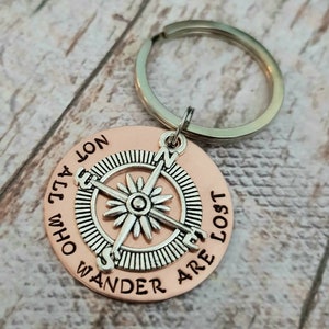 May include: A copper-colored keychain with a compass design and the engraved text "Wander who all are lost, not all who wander are lost".