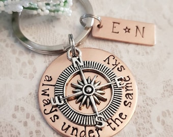 May include: Copper compass keychain with the words "Always under the same sky" engraved around the compass. A separate copper tag is attached to the keychain with the initials "E*N" engraved on it.