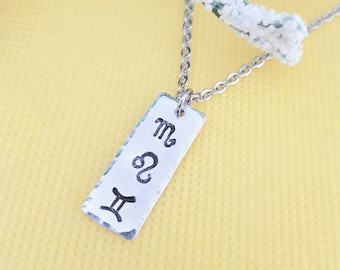 May include: Silver necklace with a rectangular pendant featuring the astrological symbols for Gemini, Leo, and Scorpio.