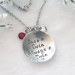 May include: Silver necklace with a round pendant that says "Once a Twin Always a Twin" with a small heart charm and a red gemstone.