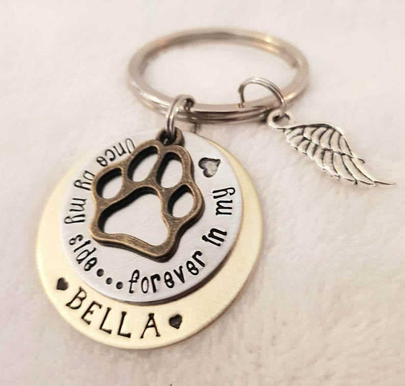 May include: Silver and gold tone keychain with a paw print charm, a small heart charm, and a small angel wing charm. The keychain has the text "Once you enter my life...forever in my heart" and "BELLA" on it.