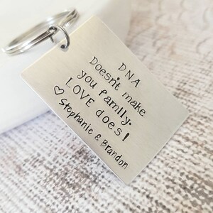 May include: Silver keychain with the text "DNA doesn't make family. LOVE does! Stephanie & Brandon" engraved on a rectangular tag.