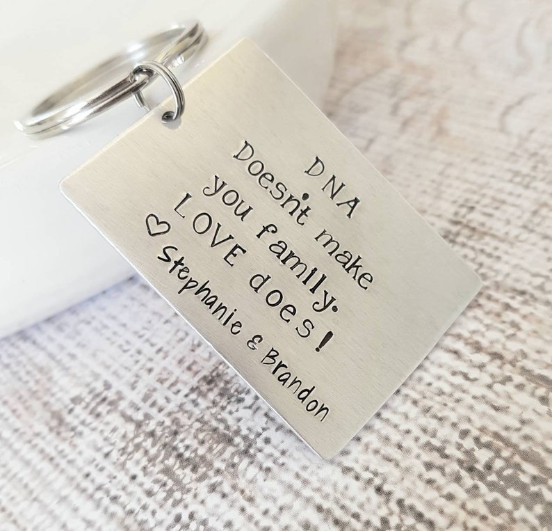 May include: Silver keychain with the text "DNA doesn't make family. LOVE does! Stephanie & Brandon" engraved on a rectangular tag.