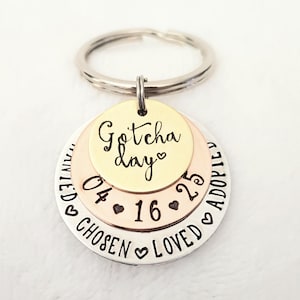 May include: A silver, gold, and copper layered keychain with the words "Gotcha Day" and the date "04-16-25". The keychain also has the words "Loved, Adopted, Chosen" engraved on it.