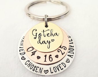 May include: A silver, gold, and copper layered keychain with the words "Gotcha Day" and the date "04-16-25". The keychain also has the words "Loved, Adopted, Chosen" engraved on it.