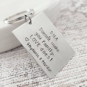May include: Silver keychain with a rectangular tag that reads "DNA doesn't make you family. LOVE does! Stephanie & Brandon".