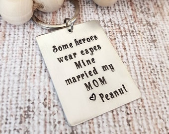 May include: Silver keychain with the text "Some heroes wear capes Mine married my MOM  Peanut"