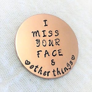 May include: A copper-coloured round disc with the text "I miss your face & other things" engraved on it. Two small hearts are included in the text.