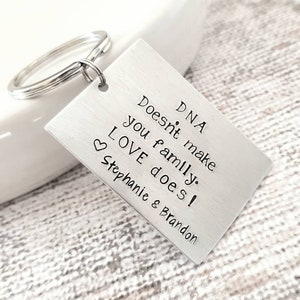 May include: Silver keychain with a rectangular tag that reads "DNA Doesn't make you family. LOVE does! Stephanie & Brandon".