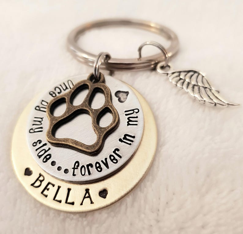 May include: A silver and gold keychain with a paw print charm, a small angel wing charm, and the text "Once my paw prints side...forever in my heart" and "BELLA".