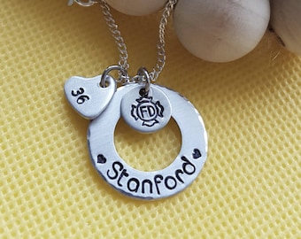 May include: Silver necklace with a heart charm engraved with "36" and a round charm with the text "Stanford" and a fire department logo with the letters "FD".