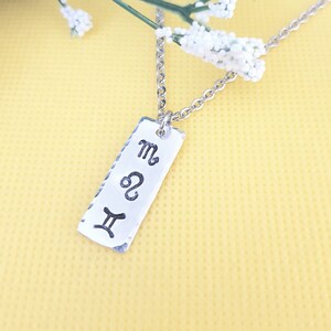 May include: Silver necklace with a rectangular pendant featuring the astrological symbols for Gemini, Leo, and Scorpio.