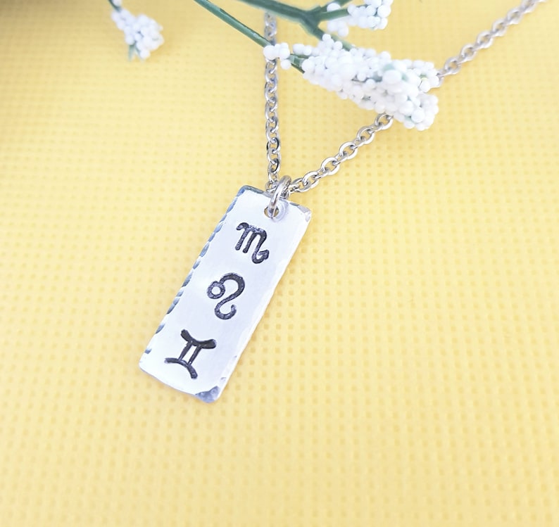 May include: Silver necklace with a rectangular pendant featuring the astrological symbols for Gemini, Leo, and Scorpio.
