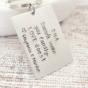 May include: Silver keychain with a rectangular tag that reads "DNA doesn't make family. LOVE does!" with a heart and the names Stephanie & Brandon.