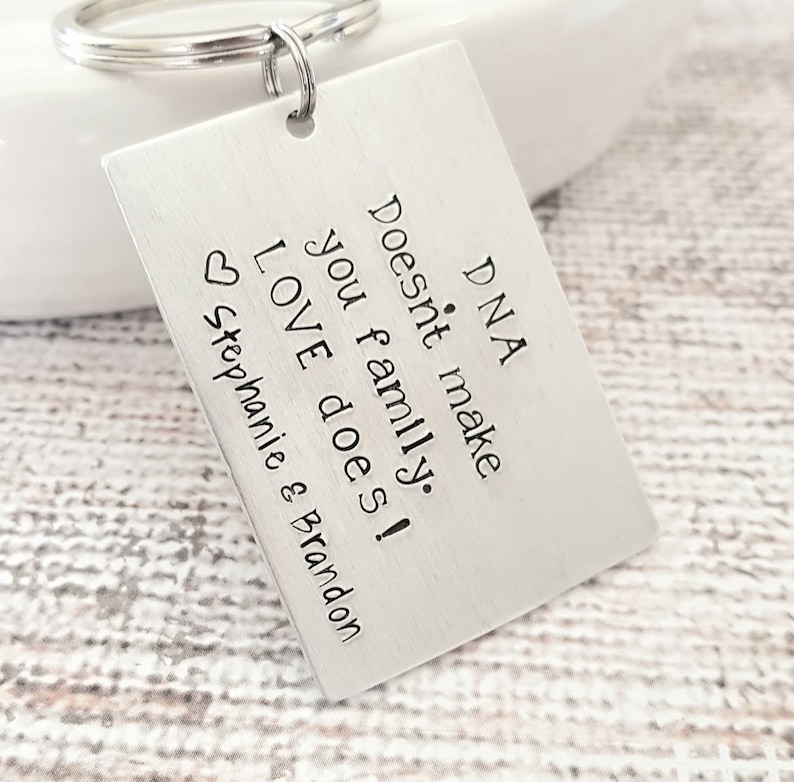 May include: Silver keychain with a rectangular tag that reads "DNA doesn't make family. LOVE does!" with a heart and the names Stephanie & Brandon.