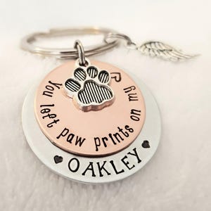 May include: Silver and copper tone keychain with a paw print charm and the text "You left paw prints on my fu" and "OAKLEY" on the bottom.