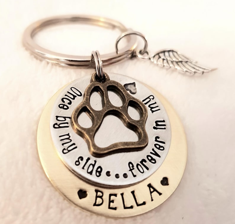 May include: A silver key chain with a gold-toned charm featuring a paw print and the text "Once by my side...forever in my heart" and the name "BELLA".