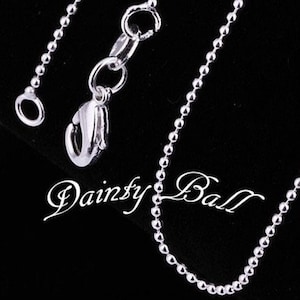 May include: A silver chain necklace with a lobster clasp closure. The chain is made of small, round beads.
