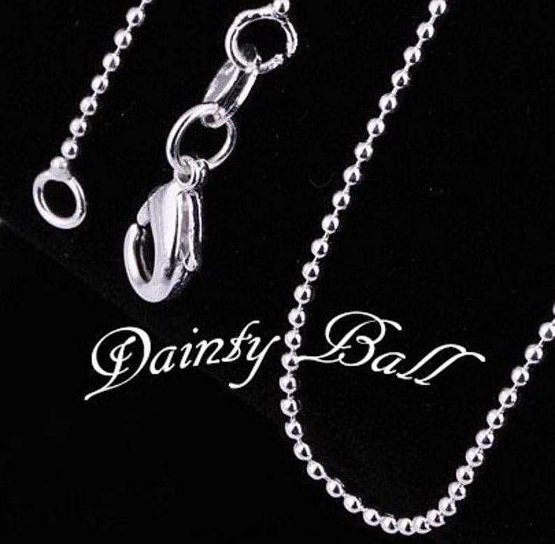 May include: A silver chain necklace with a lobster clasp closure. The chain is made of small, round beads.