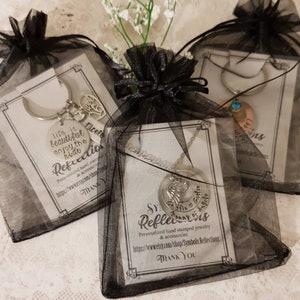 May include: Three black organza bags with silver jewelry inside. The bags are tied with black ribbon. The jewelry includes a necklace with a charm that says "Mommy of Angels", a keychain with a charm that says "Life is beautiful enjoy the ride", and a charm bracelet with a charm that says "Nicole".