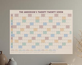 May include: A horizontal wall calendar titled THE ANDERSON'S TWENTY TWENTY SEVEN, featuring a grid layout for the year. The design includes rows for months and columns for days, with alternating pastel colored blocks in pink, yellow, blue, and green.
