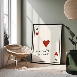May include: A printable wall art design featuring a stylized ace of hearts playing card with the text "how lucky are we?" in black script.