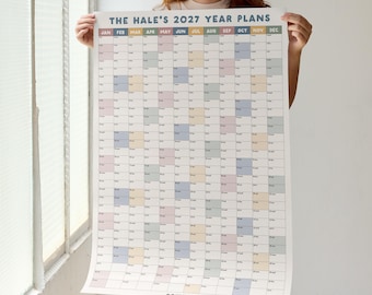May include: A large vertical wall calendar titled THE HALE'S 2027 YEAR PLANS. The grid features twelve columns for months, each with rows for days. The design uses a soft color palette of muted blue, pink, yellow, and green blocks for dates.