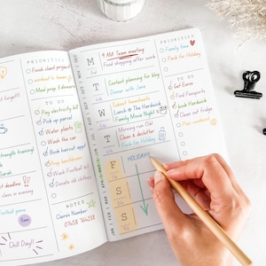 May include: A planner with handwritten notes and to-do lists. The planner includes sections for priorities, notes, and a calendar. A hand with a pencil is writing on the page. The planner is open to a page with a calendar.