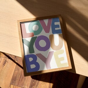 K&ouml;nnte beinhalten: Ein gerahmter Druck mit den Worten "LOVE YOU BYE" in bunten, &uuml;berlappenden Buchstaben auf wei&szlig;em Hintergrund.