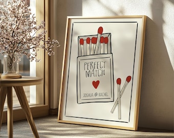 May include: A white framed print with a hand-drawn illustration of a box of matches with the text "Perfect Match" and a red heart. The names "Joshua & Rachel" are written below the heart.