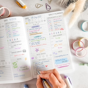 May include: A daily planner open to two pages, filled with handwritten notes and colourful highlights. The left page shows appointments and a meal planner. The right page features a daily planner with to-do lists and daily goals. Includes washi tape and pens.