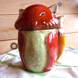 May include: A ceramic fox cookie jar with a red, orange, and green glaze. The lid is shaped like a fox's head.