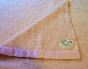 Op de afbeelding: Een lichtroze wollen deken met een roze satijnen rand en een label met de tekst "Marshall & Snelgrove, Gevestigd in 1897, Birmingham".