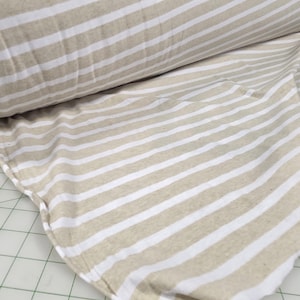 May include: Tan and white striped fabric, rolled and spread out. The fabric has a repeating pattern of horizontal stripes. The material appears to be a soft, woven textile, suitable for various sewing projects.