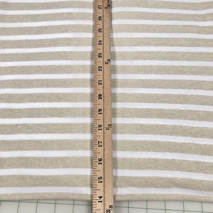 May include: Tan and white striped fabric with a wooden ruler measuring 30 inches. The fabric has horizontal stripes, with alternating tan and white bands. The ruler is positioned vertically, showing inch measurements.